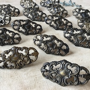 May include: Ornate antique bronze drawer pulls with decorative scrollwork. The hardware features a central medallion design and comes with mounting screws. These vintage-style pulls are ideal for cabinets and furniture.