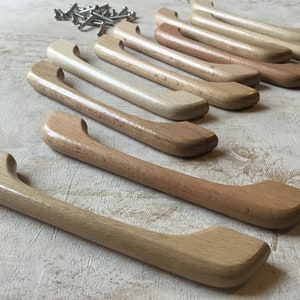 Puede incluir: Una fila de tiradores de armario de madera en varios tonos de marrón claro, dispuestos en un patrón escalonado sobre una superficie gris claro.