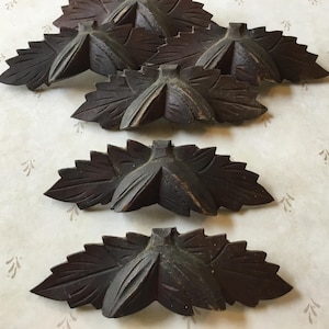 Puede incluir: Una colección de decoraciones de hojas de madera tallada de color marrón oscuro. Las hojas tienen vetas detalladas y un diseño tridimensional. Estos elementos decorativos son probablemente para muebles o proyectos de artesanía.