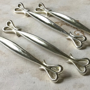 Może przedstawiać: Pięć srebrnych gałek do szuflad z sercowatym wzorem. Gałki są wszystkie tego samego rozmiaru i kształtu, a ich powierzchnia jest polerowana.