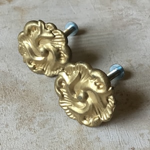 May include: Two gold-toned cabinet knobs with a floral design and a screw attachment.
