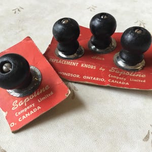 May include: Four black wooden replacement knobs with silver metal bases and a star-shaped design. The knobs are packaged on red cards with white text that reads "Star Replacement Knobs by Sapoline Company Limited Windsor, Ontario, Canada".