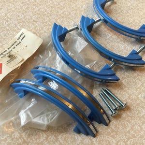 Peut inclure: Un ensemble de six poignées de placard bleues vintage avec des accents argentés et des vis de montage. Les poignées ont un design incurvé et sont faites d'un matériau brillant. Une étiquette en papier vintage est également incluse.