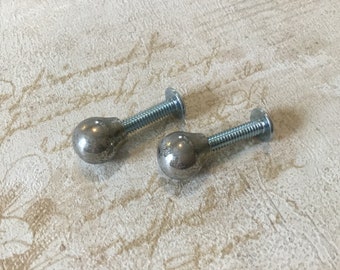 Puede incluir: Dos pomos de metal plateado con forma de bola redonda y rosca de tornillo. Los pomos están sobre un fondo blanco.
