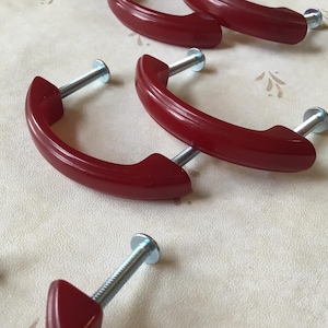 May include: Five red plastic drawer pulls with silver screws. The pulls are shaped like a half-circle with a rounded edge.