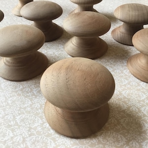 May include: Several unfinished wooden knobs, each with a mushroom design. The knobs are light brown and have a smooth, rounded top and a wider base. They are arranged on a patterned surface, possibly for a craft or home improvement project.