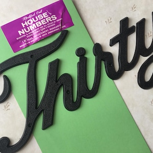May include: Black plastic house number "Thirty" in a cursive font. The number is on a green background with a white sticker that says "Spelled Out House Numbers".