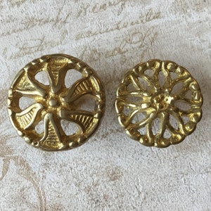 May include: Two gold-toned metal decorative knobs with intricate floral designs. The knobs have a circular shape and a raised center.