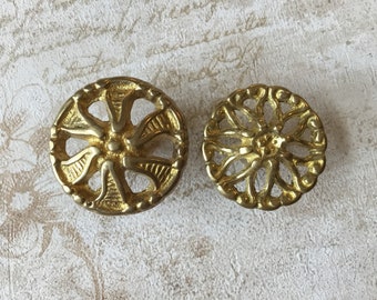 May include: Two gold-toned metal decorative knobs with intricate floral designs. The knobs have a circular shape and a raised center.