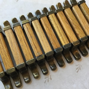 May include: A set of 12 wooden cabinet pulls with brass accents. The pulls are rectangular with a slightly curved shape and have a wood grain finish. The brass accents are on the ends of the pulls and have a shiny finish.