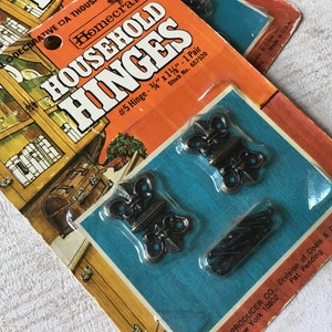 Puede incluir: Paquete de dos bisagras de latón de estilo antiguo con adornos decorativos. Las bisagras miden 3/4 de pulgada por 1 1/4 de pulgada y vienen con tornillos. El paquete está etiquetado con "Household Hinges #5 Hinge - 3/4" x 1 1/4" - 1 Pair Stock No. 657520" y "Producer Co., Division of Coats & Clark Inc. New York 10802 Pat. Pending Made in U.S.A."