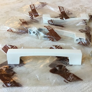 May include: Four white plastic cabinet door pulls with a brown label that says "SCOW" on each. The pulls are packaged in clear plastic bags.