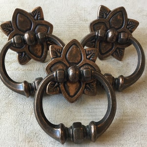 May include: Three antique bronze drawer pulls with a floral design and a ring handle.