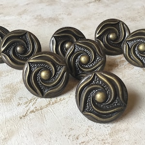 May include: Eight antique brass cabinet knobs with a swirling design. Each knob has a raised centre circle.