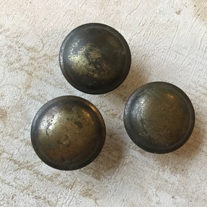 Peut inclure: Trois boutons ronds en métal pour armoire avec une finition vieillie et patinée. Les boutons sont de couleur bronze foncé avec une touche d'or.