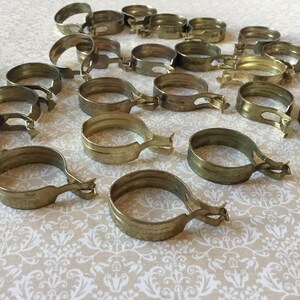 Peut inclure: Plusieurs colliers de serrage en laiton vintage, disposés sur une surface à motifs. Chaque collier est circulaire avec un levier. Le laiton présente une patine chaude et vieillie. Idéal pour projets de restauration.