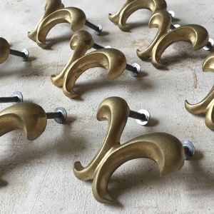 Puede incluir: Ocho pomos de armario de metal dorado con un diseño decorativo, ornamentado y en forma de rollo. Cada pomo tiene un solo tornillo para la instalación.