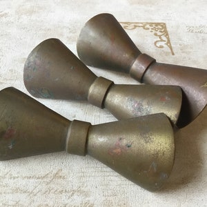 Puede incluir: Tres tazas medidoras de latón con forma cónica y base acampanada. Las tazas están desgastadas y tienen un acabado patinado.