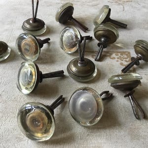 May include: A collection of 12 vintage glass cabinet knobs with metal hardware. The knobs are clear glass with a slight iridescent sheen. The metal hardware is a mix of brass and silver tones.