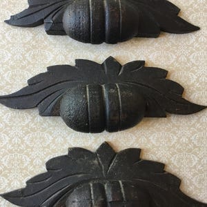 Puede incluir: Tres tiradores de cajón de hierro fundido negro con diseño de hojas. Cada tirador presenta una esfera central texturizada con ranuras verticales, flanqueada por hojas estilizadas. El herraje es probablemente para restauración de muebles o uso decorativo.