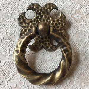 May include: A brass door pull with a twisted ring handle and a decorative, textured, four-leaf clover design.