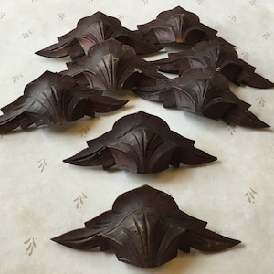 Puede incluir: Una colección de ocho adornos de esquina de madera tallada de color marrón oscuro. Cada pieza presenta un diseño de hoja estilizada con vetas detalladas. Los adornos están dispuestos sobre una superficie de color claro con un patrón sutil.