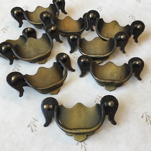 May include: Eight antique brass cabinet pulls with black metal accents. The pulls have a decorative, ornate design.