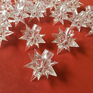 May include: A collection of clear, multi-faceted star-shaped plastic light covers. Each piece features a central cylindrical opening for a bulb, with numerous sharp, pointed rays radiating outward in a geometric, crystalline design.