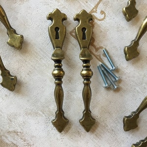 Könnte beinhalten: Zwei antike Messing-Schranktürgriffe mit Schlüssellochausschnitten und verzierten Designs. Die Griffe sind etwa 10 cm lang und werden mit Schrauben zur Montage geliefert.