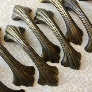 May include: A set of antique brass cabinet handles. Each handle has a fluted design with a curved grip and decorative ends. The handles have a vintage, aged appearance, suggesting they are old or have been aged.