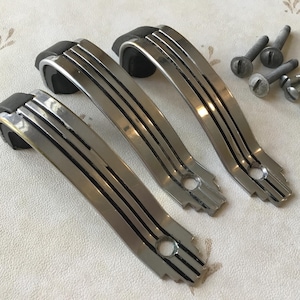 Peut inclure: Trois poignées de porte de placard argentées avec des accents noirs et un design géométrique. Les poignées sont courbées et ont une finition lisse et polie.