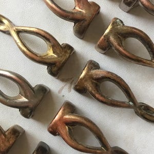 Op de afbeelding: Een verzameling van acht antieke metalen ladegrepen met een gedraaid ontwerp. De grepen zijn in verschillende tinten goud en zilver.