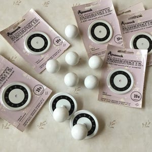 May include: A close-up of a set of white plastic knobs with black trim. The knobs are labelled "Amerock Fashionette" and have a diameter of 5 cm. The knobs are packaged in clear plastic bags with a price tag of 39 pence.