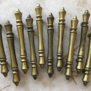 Puede incluir: Un juego de 12 tiradores de cajón de armario de color dorado antiguo con un diseño decorativo. Los tiradores son de metal y tienen un acabado ligeramente desgastado.