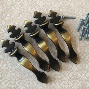 May include: Set of five antique-style cabinet pulls with a dark bronze finish and brass accents. Each pull features a decorative top and a curved handle. Mounting screws are included.