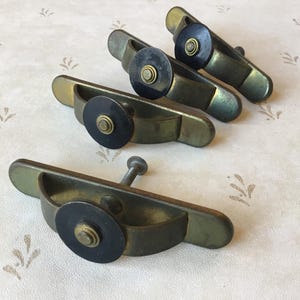 Könnte beinhalten: Vier antike Messing-Schrankgriffe mit schwarzen runden Knöpfen. Die Griffe haben die Form eines Halbkreises mit einer Schraube auf der Rückseite.