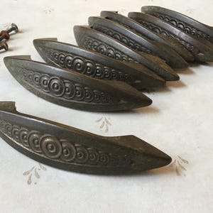 Può includere: Un set di otto tiretti per armadi in bronzo antico con un motivo circolare decorativo. I tiretti sono in buone condizioni con una finitura patinata.
