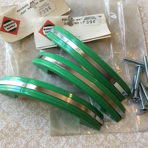 Peut inclure: Ensemble de trois poignées de placard vertes vintage avec des accents argentés, ainsi qu'un sachet de vis. Les poignées ont un design incurvé et sont encore dans leur emballage d'origine avec l'étiquette Winnipeg Supply.
