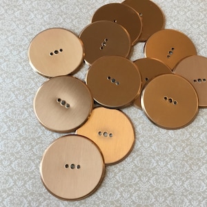 Peut inclure: Un ensemble de gros boutons ronds de différentes nuances d'or et de bronze. Chaque bouton comporte trois petits trous pour la couture. Les boutons sont dispersés sur une surface claire à motifs.