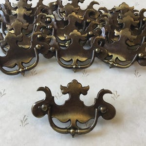 May include: A group of 11 antique brass drawer pulls with ornate, decorative designs. The pulls have a traditional, vintage style and are perfect for adding a touch of elegance to any home.