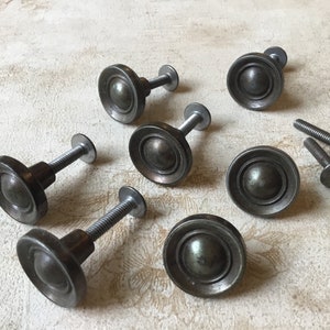 Könnte beinhalten: Acht silberne Metall-Schrankknöpfe mit einem erhabenen runden Design. Die Knöpfe haben eine abgenutzte Oberfläche und werden mit Schrauben geliefert.