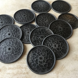 May include: A collection of 12 black metal decorative round discs with a textured surface and a small hole in the centre.