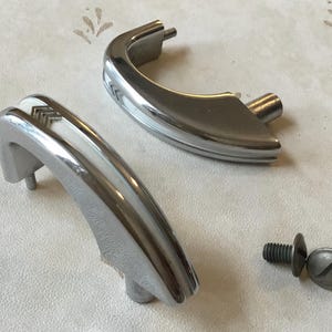 May include: Two chrome-plated door handles with white plastic inserts. The handles are shaped like a half-circle and have a decorative design on the plastic inserts. A single chrome-plated screw is also included.