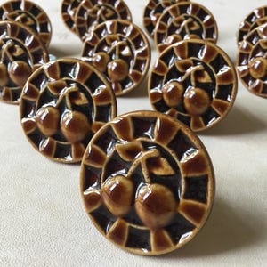 Peut inclure: Ensemble de boutons de meubles en céramique marron. Chaque bouton présente un motif de cerise au centre, entouré d'une bordure décorative. Les boutons sont ronds et ont une finition brillante, parfaits pour ajouter une touche vintage aux meubles. (Mesures en cm)