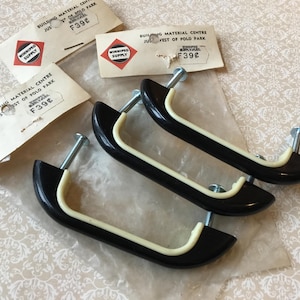 May include: Four black and cream cabinet pulls with silver fixings are shown. The pulls have a curved design with a cream accent. The image also shows three vintage price tags with the text "WINNIPEG SUPPLY".