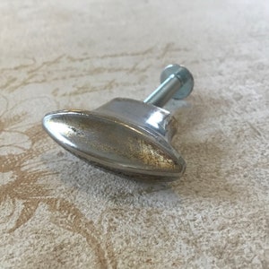 May include: A silver oval-shaped cabinet knob with a screw. The knob has a slightly worn finish.