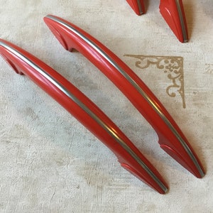 May include: Two red plastic cabinet door handles with silver trim. The handles are curved and have a modern design.