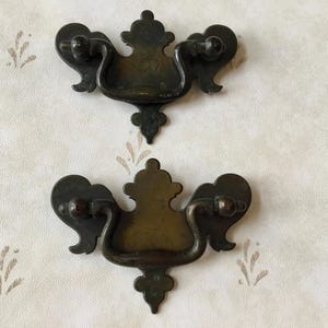 Puede incluir: Dos tiradores de cajón de latón antiguo con diseños ornamentados. Cada tirador tiene una manija curva y una base decorativa en forma de flor.