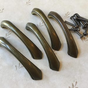 Può includere: Cinque maniglie per ante di armadio in ottone antico con un design curvo. Le maniglie hanno una patina scura e sono in buone condizioni.