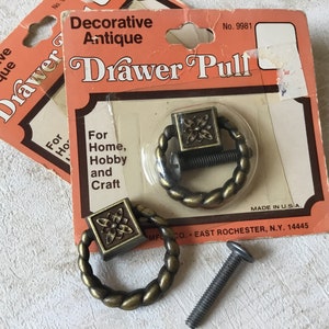 Puede incluir: Dos tiradores de cajón de oro antiguo con un diseño floral decorativo. Los tiradores están empaquetados en una tarjeta que dice "Decorative Antique Drawer Pull" y "For Home, Hobby and Craft".